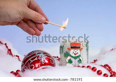 Person lighting cheerful Christmas candle with festive decorations around it and plain background