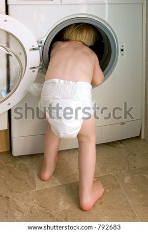 Young child in nappy climbing inside a white washing machine