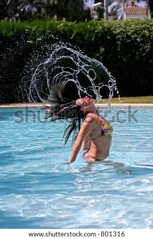 Woman or girl throwing hair back fast in sunny, blue swimming pool. Water frozen as it flies from her hair.
