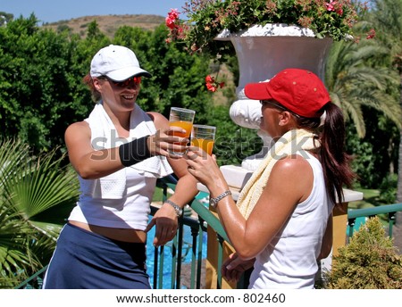 Two young, attractive, fit, tanned and healthy women drinking and toasting each other with orange juice after a hot game of tennis in the sun on vacation.