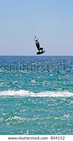 Extreme sports with kitesurfer enjoying vacation, flying high through the air over the ocean as his kite hits some serious wind.