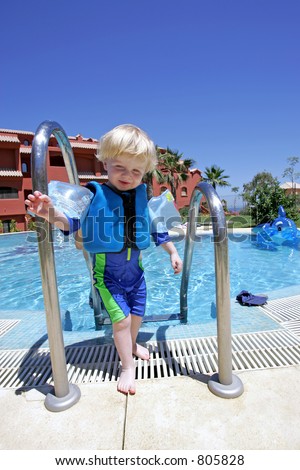 Young boy climbing out of swimming pool on vacation with arm bands and a UV suit on