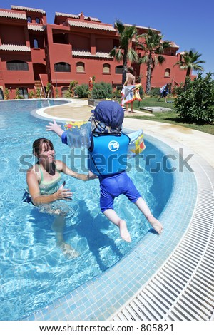 Mother helping her young son to swim and jump in a sunny swimming pool on vacation in Spain