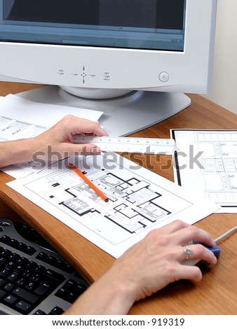 Close up of person working on a computer or PC Plans of a house a ruler and pencil are on the wooden desk
