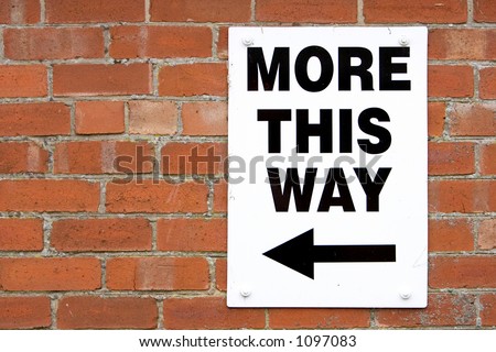 Sign on brick wall of farm saying More This Way with a black arrow pointing to the left