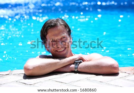 Smiling man lying on side of swimming pool in the sun on vacation