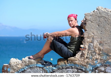 Handsome middle aged man sitting on an old stone wall in the sun