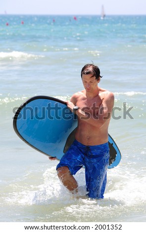 Handsome, fit middle aged man carrying surfboard on sandy beach in summer during vacation or holiday