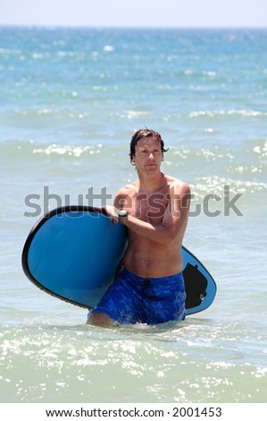 Handsome, fit middle aged man carrying surfboard on sandy beach in summer during vacation or holiday
