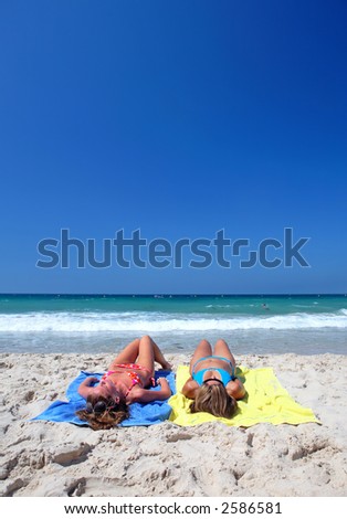 Two young attractive women chilling on a sunny beach on holiday or vacation by the sea