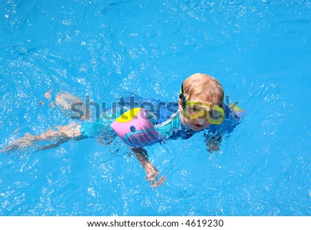 Young Boy in blue Swimming Pool on Vacation with goggles arm bands and a uv protection suit