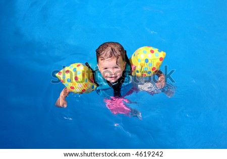 Baby girl floating on top of swimming pool in flotation jacket and arm bands