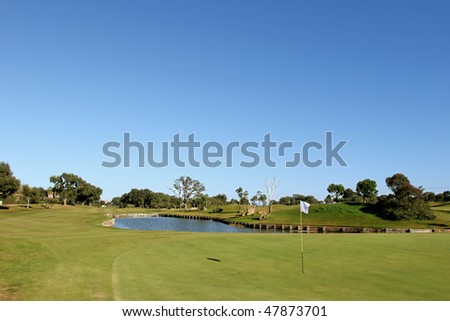 Green, flag and water feature on a sunny golf course with clear blue sky
