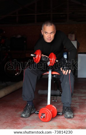 Handsome fit middle aged man doing exercises with red dumbbells or weights in his garage gymnasium