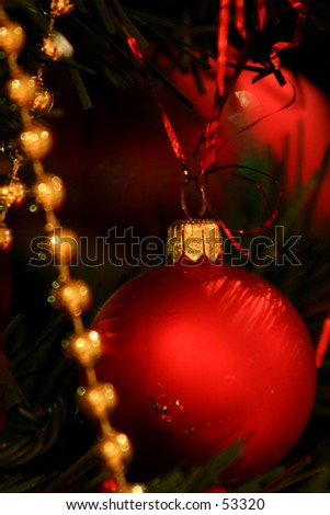 Red bauble with gold clasp on a tree, with a gold string of beads in the foreground