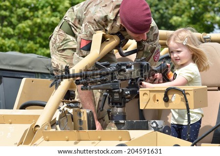 Military Tattoo  COLCHESTER ESSEX UK 8 July 2014:   Small Girl being shown gun by soldier