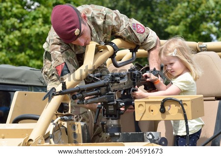 Military Tattoo  COLCHESTER ESSEX UK 8 July 2014:   Small Girl being shown machine gun by soldier