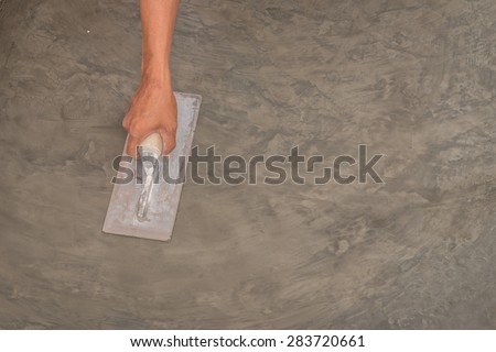 Close up of hand using steel trowel to finish wet concrete floor of polished concrete surface