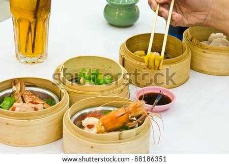 Hand holding chopsticks reaching out for Dim Sum food in restaurant.