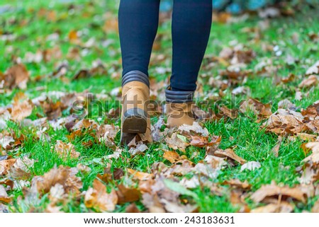 Autumn fall concept with colorful leaves and boots outside. Close up of woman feet walking in boots.