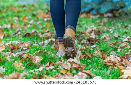 Autumn fall concept with colorful leaves and boots outside. Close up of woman feet walking in boots.