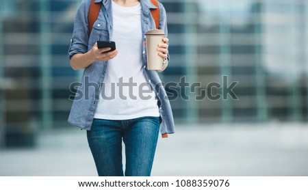 Woman use mobile phone walking with coffee themo cup in hand