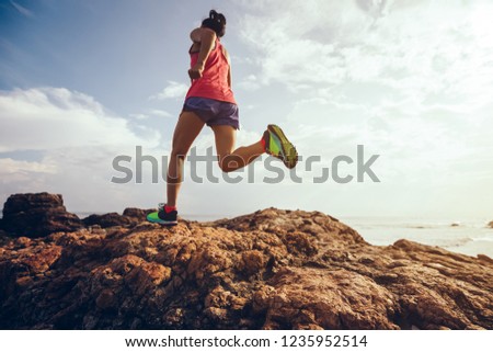 Young fitness woman trail runner running to rocky mountain top on seaside