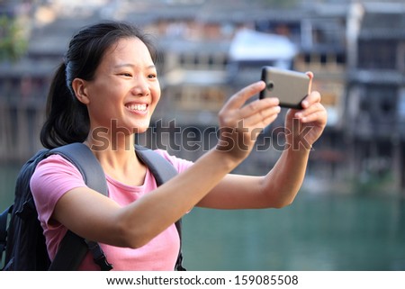 young asian woman use cell phone taking photo at fenghuang ancient town,china