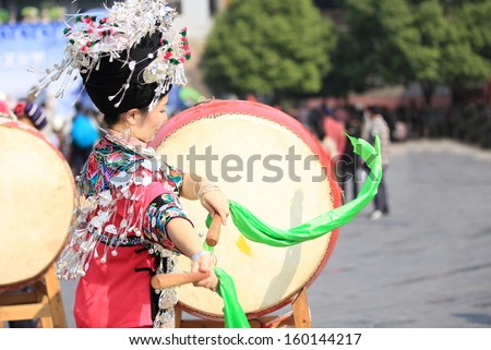 FENGHUANG - OCT 13:Miao nationality womon wearing silver accessories on hair and clothes beats a drum to celebrate the local festival in fenghuang ancient town on Oct 13, 2013 in Fenghuang,China.