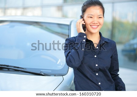 beautiful asian businesswoman on the phone leaning on car outside of office building