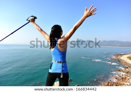cheering hiking woman stand seaside rock looking the view with arms open