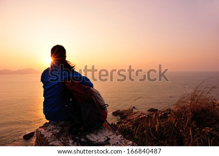 hiking woman sit on mountain rock watching the sunrise at the sea