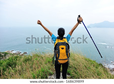 cheering woman hiker open arms to the sea stand at mountain peak