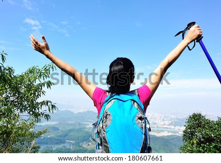 cheering woman hiker with her arms raised on mountain peak