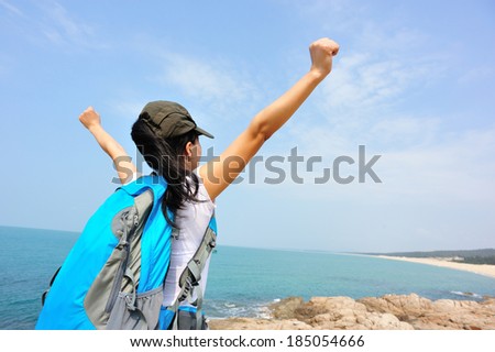 cheering hiking woman open arms at seaside rock looking at the view
