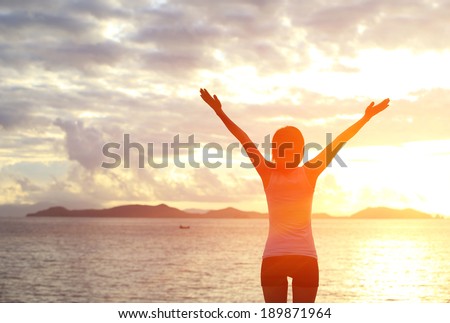cheering woman open arms to sunrise at sea