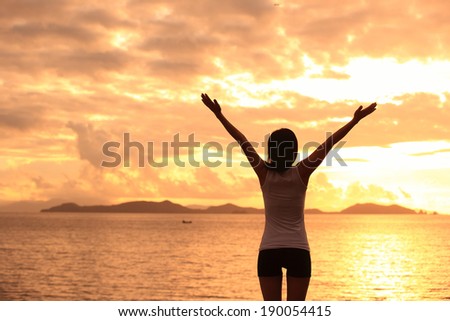 cheering woman open arms to sunrise at sea