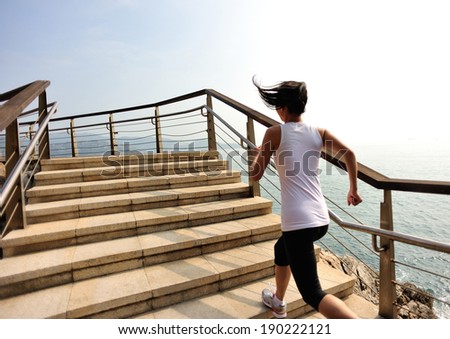 Runner athlete running on seaside stone stairs. woman fitness jogging workout wellness concept.