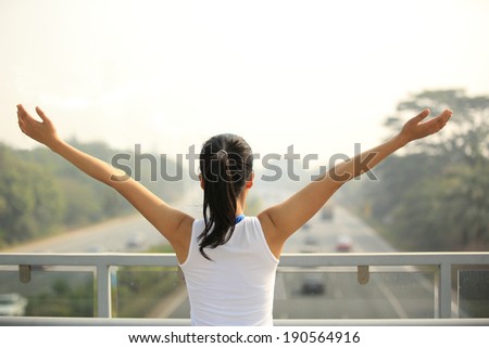 sporty woman stand at the pedestrian overpass open arms to the rush driveway in modern city