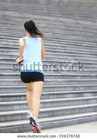 Runner athlete running on stairs. listening to music in headphones from smart phone mp3 player smart phone armband.woman fitness jogging workout wellness concept.