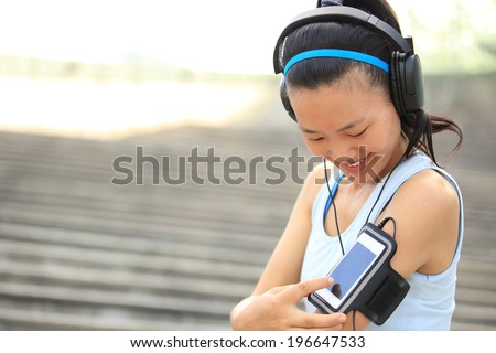 Runner athlete listening to music in headphones from smart phone mp3 player smart phone armband.woman fitness jogging workout wellness concept.