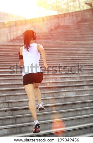 Runner athlete running on stairs. listening to music in headphones from smart phone mp3 player smart phone armband.woman fitness jogging workout wellness concept.