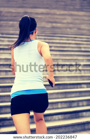 Runner athlete running on stairs. listening to music in headphones from smart phone mp3 player woman fitness jogging workout wellness concept.