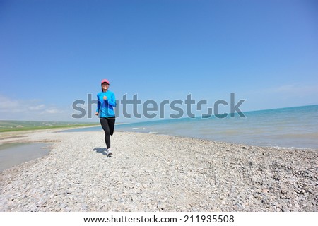 Runner athlete running on stone beach of qinghai lake. woman fitness jogging workout wellness concept.