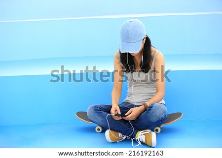 woman skateboarder sit on skatepark stairs listening music from smart phone mp3 player