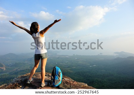 cheering woman hiker open arms at mountain peak