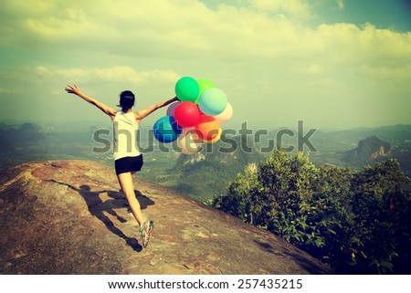 young asian woman running on mountain peak rock with colored balloons