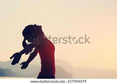 young woman open arms under the sunrise at seaside