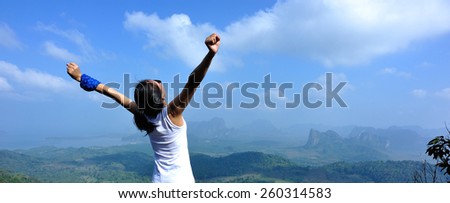 young woman cheering open arms at mountain peak