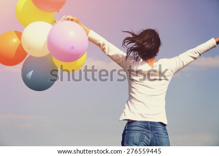 young asian woman running and jumping on green grassland with colored balloons